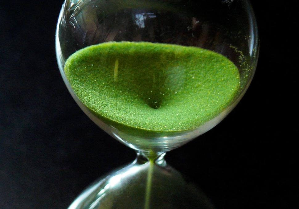 Close up of an hourglass. Green sand is falling to the bottom.