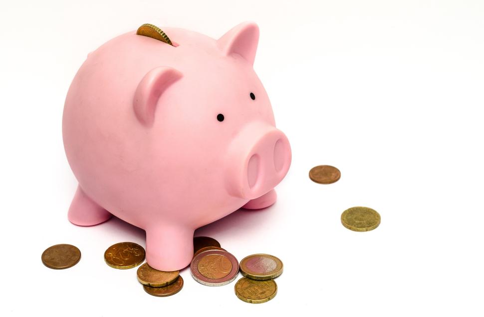 Pink piggy bank with several coins at its feet and one in the slot in the top of the body